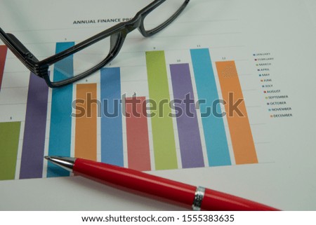 Close up of working table with eye glasses,pen and paper of graph chart report.Finance business concept. Selective focus.