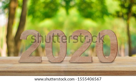 Happy new year 2020 wooden number on wood table with sunlight and green bokeh background.