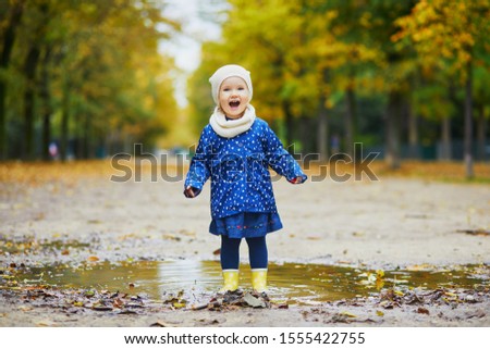 Child wearing yellow rain boots and jumping in puddle on a fall day. Adorable toddler girl having fun with water and mud in park on a rainy day. Outdoor autumn activities for kids Royalty-Free Stock Photo #1555422755
