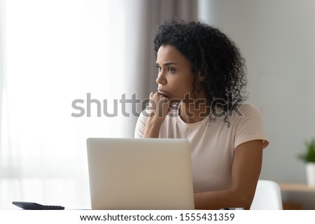 Thoughtful African American woman using laptop, pondering task or strategy, looking in distance, student freelancer working on difficult project at home, pensive girl taking break, planning Royalty-Free Stock Photo #1555431359