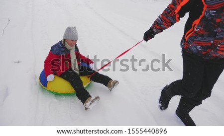 Happy dad rides a child on sled on a white snowy road. Christmas Holidays. A fun game for adults and children. The concept of a happy family. A teenager rides in Tubing