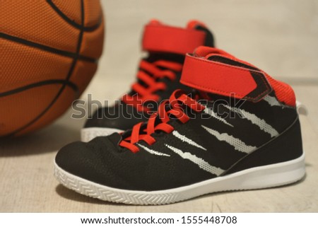 Red and black basketball sneakers close-up on a background of an orange basketball ball on a light background with selective focus.