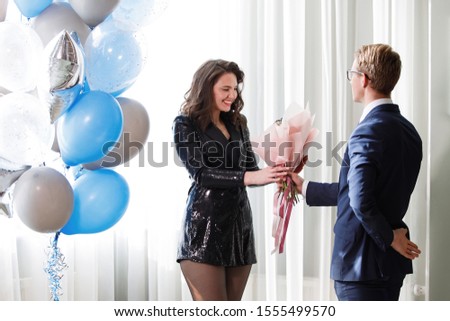Man gives a bouquet of flowers to a girl indoors. Holiday surprise. Birthday present.
