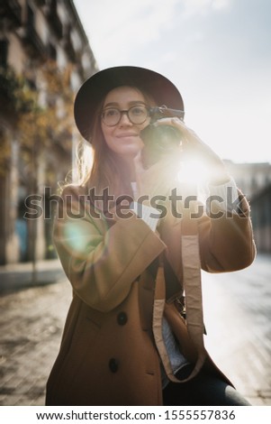Photographer in glasses with retro photo camera. Tourist portrait. Girl in hat travels in Barcelona holiday. Sunlight flare street in europe city. Traveler hipster shooting architecture, copy space