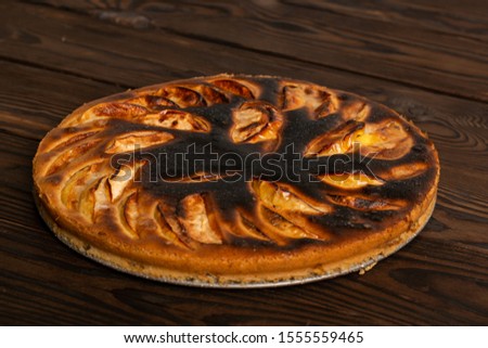 failed apple pie. burnt on top and the dough did not rise during baking. textured burnt pie crust. lies on a wooden table

 Royalty-Free Stock Photo #1555559465