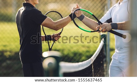 Two young man shaking hands after playing tennis. Tennis players shaking hands over the net after the match. Royalty-Free Stock Photo #1555637465