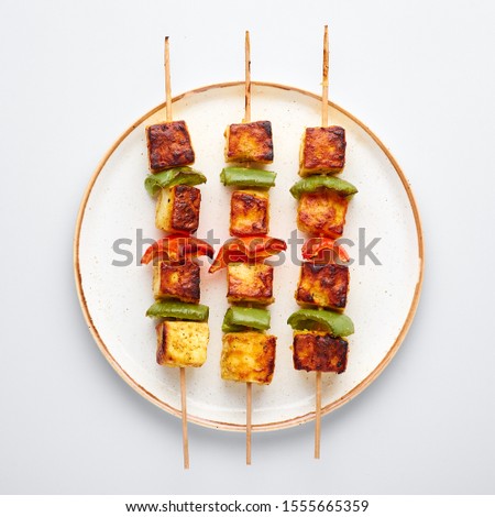 Paneer Tikka at skewers in white plate isolated at white background. Paneer tikka is an indian cuisine dish with grilled paneer cheese with vegetables and spices. Indian food. Top view Royalty-Free Stock Photo #1555665359