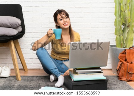 Pretty young woman sitting on the floor at indoors holding a cup of coffee