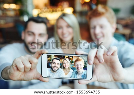 Hands of two happy guys holding smartphone while showing photo of them and pretty girl on touchscreen