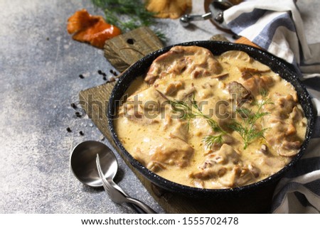 Fricassee - French Cuisine. Chicken stewed in a creamy sauce with mushrooms in a pan on a light stone background.  Royalty-Free Stock Photo #1555702478
