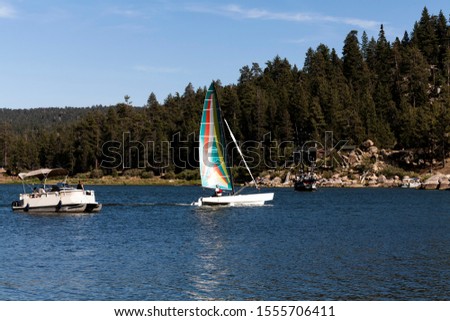 Pontoon Motorboat And Catamaran Sailboat On Big Bear Lake Southern California With Blue Sky And Trees Royalty-Free Stock Photo #1555706411