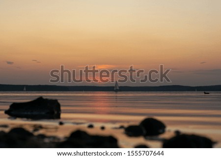 sailing boat against the pink sky after sunset. rocky shore in the foreground