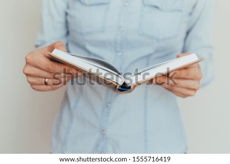Beautiful female hands are holding an open book or magazine in a room on against a light wall