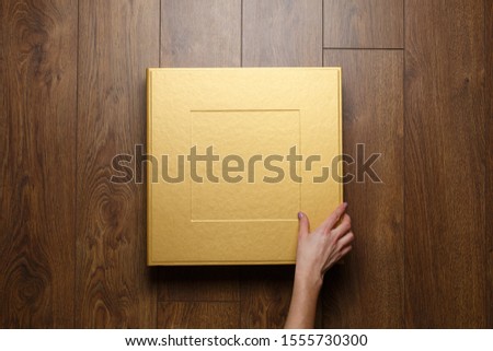 golden stylish square gift cardboard box for photo album.
leather family photo book in the open box..the person is looking at photo book.womans hand  open bright original box for white wedding album.