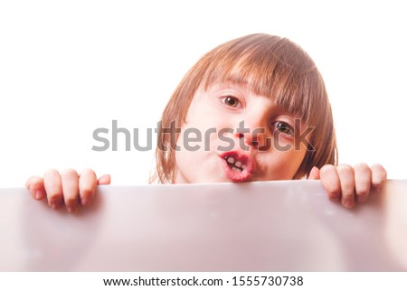 Cute little child girl looking behind white empty banner. Funny facial expression