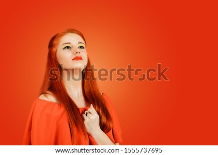 Self-esteem. Redhead woman in red dress holding hand to her chest, being proud of herself, feeling self-important, having napoleon syndrome concept isolated on a red background wearing yellow makeup Royalty-Free Stock Photo #1555737695