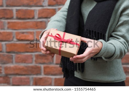 Woman in a sweater giving a christmas or birthday gift wrapped in brown paper and red ribbon. Copy space. Holiday concept