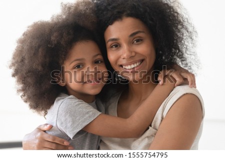 Portrait of smiling african American young mom hold in arms hug cute little mixed race daughter posing for picture together, happy biracial mother cuddle embrace small girl child looking at camera Royalty-Free Stock Photo #1555754795
