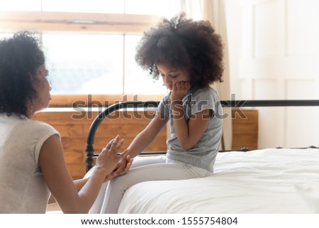 Loving african American mom caress sad hurt biracial preschooler daughter sit on bed in bedroom, caring young mixed race ethnicity mom cuddle comfort upset offended small girl child feeling depressed Royalty-Free Stock Photo #1555754804
