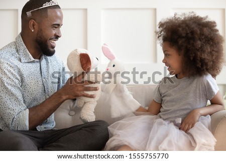Funny loving african American dad wearing plastic crown playing with cute little princess daughter, smiling biracial father have fun engaged in childish girlish game with mixed race girl child at home