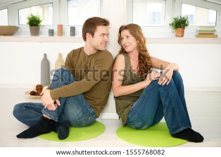 Couple sitting on floor at home resting, smiling at each other.