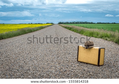 Woman’s sun hat and vintage suitcase on a country road on the prairies