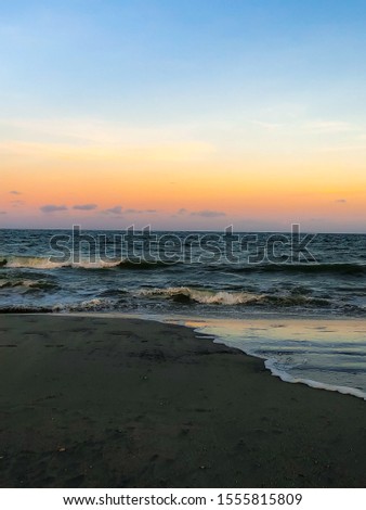 A colorful sunset reflected on calm waves crashing on the shore