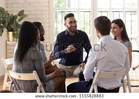 Positive people sit in circle take part in team building or therapy session, try to solve problems or do training exercise, focus on arabian man telling story share experience at group meeting concept Royalty-Free Stock Photo #1555828883