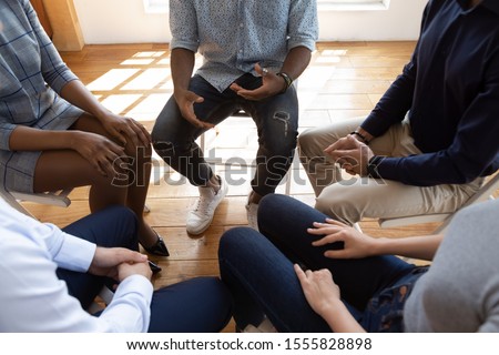 Close up top view unrecognizable multiracial workers strategizing indoors at informal atmosphere, people seated in circle talking share problems tell stories during psychological rehab session concept Royalty-Free Stock Photo #1555828898