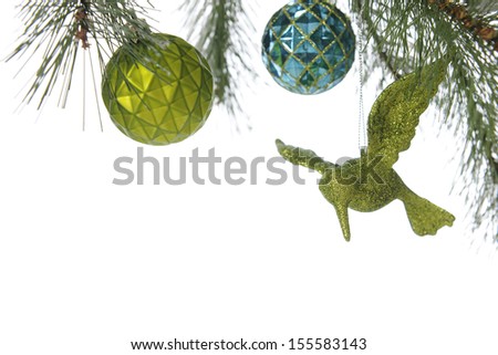 A top boarder under the boughs of a decorated Christmas tree, revealing a round green and blue bulb and a sparkly green humming bird ornament.  On a white background.