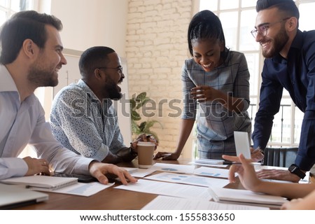 Multi racial employees laughing during briefing in boardroom, colleagues do paperwork analyze statistics financial report in charts and graphs take break having fun telling jokes enjoy pause concept Royalty-Free Stock Photo #1555833650