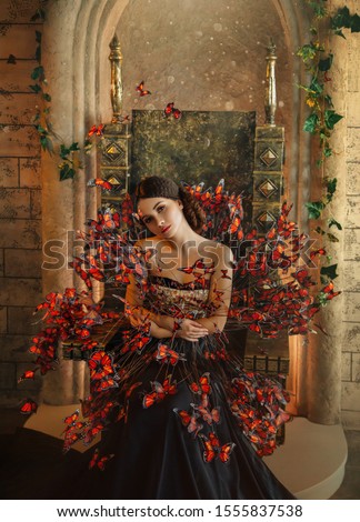 Closeup portrait. attractive woman image of queen sitting golden throne. dark black creative dress many orange butterflies. Gothic beauty  fashion Design gown. Backdrop old castle room. face princess