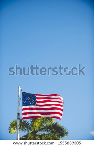 A vertical shot of the united states flag on a pole with a blue sky in the background