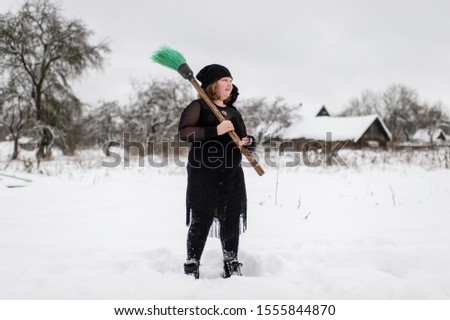 Excited girl dressed in with costume starting to gly on her broomstick to coven in snowy winter day in countryside nature.