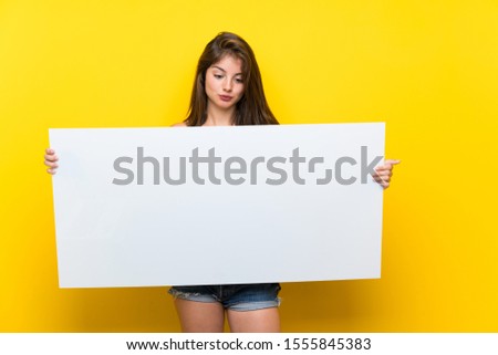 Caucasian girl in colorful dress over isolated yellow background holding an empty white placard for insert a concept