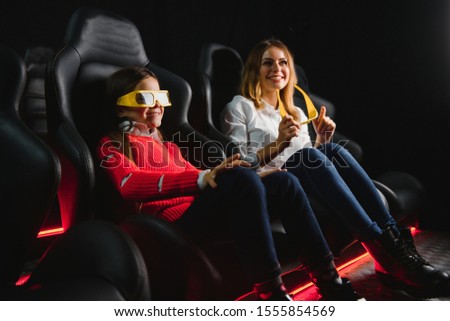 Happy mother and daughter wearing 3d glasses in cinema. Cheerful family watching funny film and enjoying spare time together in movie house. Concept of enjoyment and fun.