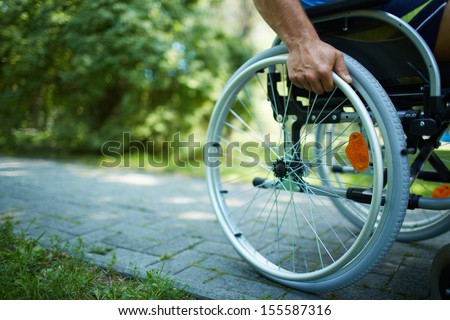 Close-up of male hand on wheel of wheelchair during walk in park Royalty-Free Stock Photo #155587316