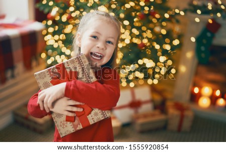 Merry Christmas and Happy Holidays! Cheerful cute child girl with gift. Kid is having fun near tree. 
