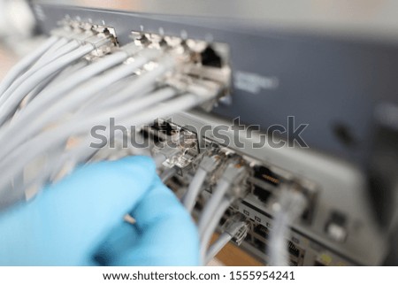 Focus on high-tech chords and ethernet cables in hand of hardworking man wearing blue glove used for right work of web router. Computer technology concept. Blurred background