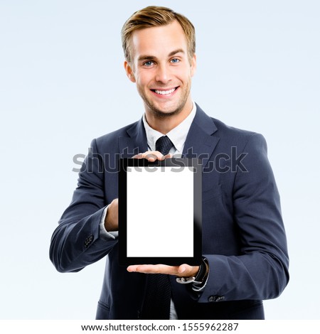 Happy smiling confident businessman showing blank noname tablet pc monitor, isolated over grey background, with copy space for some slogan or text. Success in business concept studio picture. 