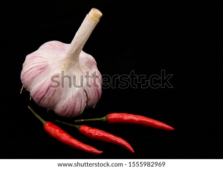 One head of garlic and three pods of red hot pepper on a black background.