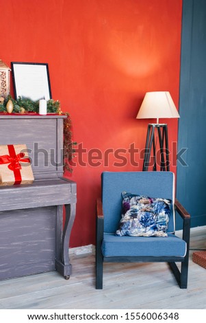 Blue armchair, floor lamp and piano on the background of red walls with Christmas decor