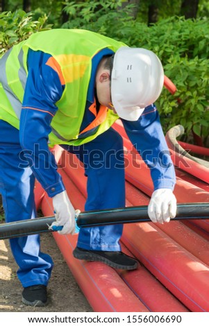 front view of a builder in a white helmet cuts off a piece of black pipe