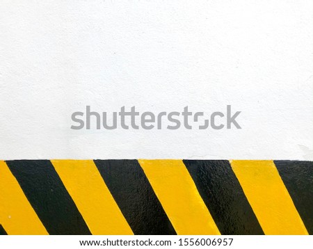 White concrete walls with the yellow and black stripes for danger warning symbol on the bottom, taken outdoors, leaving space for copies.