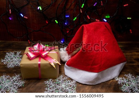 Santa Claus hat and Christmas gift. In the background a garland of multi-colored lights.