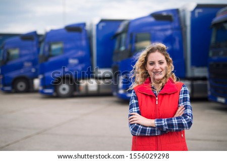 Truck driver occupation. Portrait of woman truck driver in casual clothes standing in front of truck vehicles. Transportation service. Royalty-Free Stock Photo #1556029298