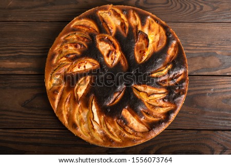 failed apple pie. burnt on top and the dough did not rise during baking. textured burnt pie crust. lies on a wooden table. view from above Royalty-Free Stock Photo #1556073764