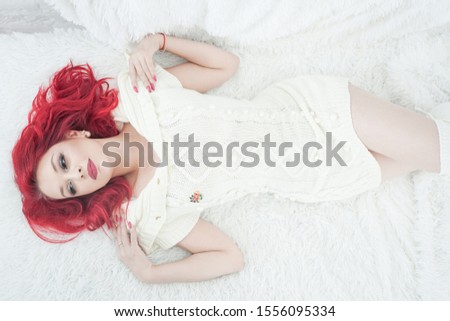 cute red hair woman in cozy knitted white sweater dress relax on the fur bed in her white room