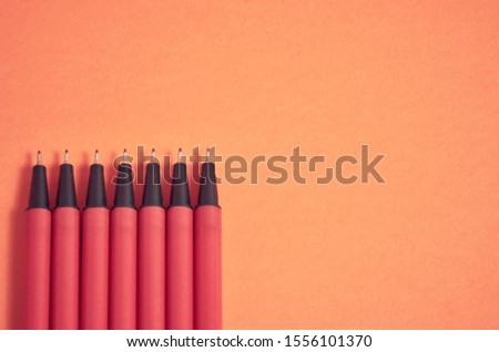 Black pencil sticks out from a of red pens without caps on against a red background.