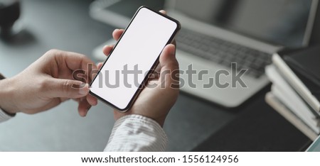 Cropped shot of professional businessman holding blank screen smartphone in dark modern office room Royalty-Free Stock Photo #1556124956